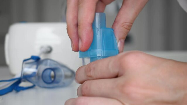 female hand close screw the lid on the measuring cup with pours saline solution for inhalation nebulizer at the table. Slow motion and close up. preparation for the procedure. inhaler parts