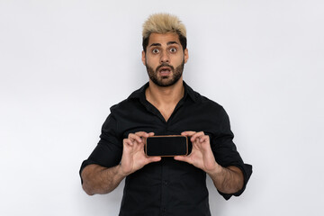 Astonished young man presenting smartphone. Male Caucasian model with brown eyes, ombre painted hair and beard in black shirt showing mobile phone screen. Advertising, modern technology concept