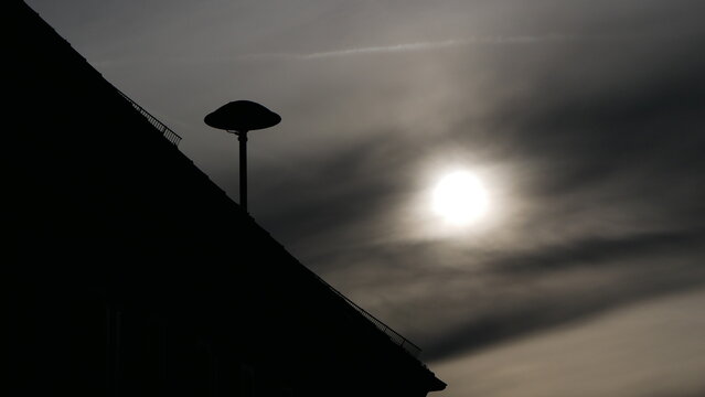 Symboldbild einer Apokalypse des Klimawandels: Eine Luftschutzsirene E57 mit einer düsteren schmierigen Sonne hinter Nebelwolken im Gegenlicht