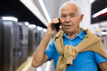 Elderly man using mobile phone while waiting for train in platform of underground station