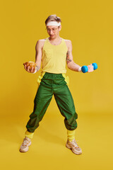 Fototapeta na wymiar Choice. Portrait of young cheerful man in sports uniform with croissant and dumbbell over bright yellow studio background. Concept of emotions, facial expression, sportive lifestyle, retro fashion. Ad