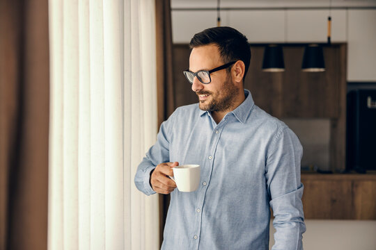 A smart casual businessman drinks his coffee and looks trough the window.