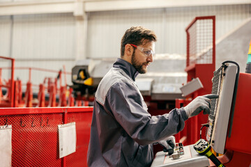 Profile of a metallurgy worker maneuvering machine and pressing buttons in facility.