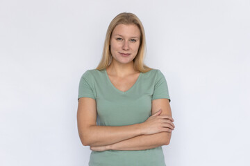 Fototapeta premium Positive woman with arms crossed. Young female model standing crossing arms and smiling. Portrait, studio shot, confidence concept