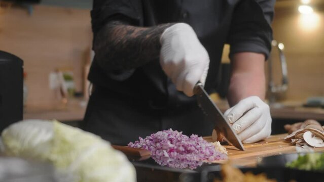 Mushroom being sliced on a wooden board by professional chef in an elegant black shirt with tattoos and white gloves.
A modern, fancy looking kitchen with fresh vegetables besides Cinematic Sliding 4K