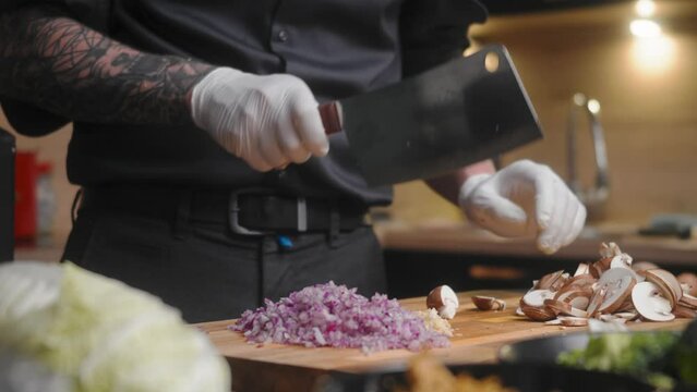 Mushroom being sliced on a wooden board by professional chef in an elegant black shirt with tattoos and white gloves.
A modern, fancy looking kitchen with fresh vegetables besides Cinematic Sliding 4K