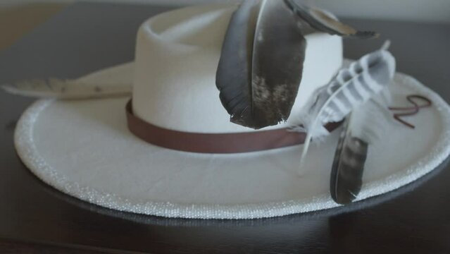 Native American hand beaded hat. Indigenous fashion. Personalized vintage white hat with black and white feathers, brown ribbon around. Stabilized handheld shot.