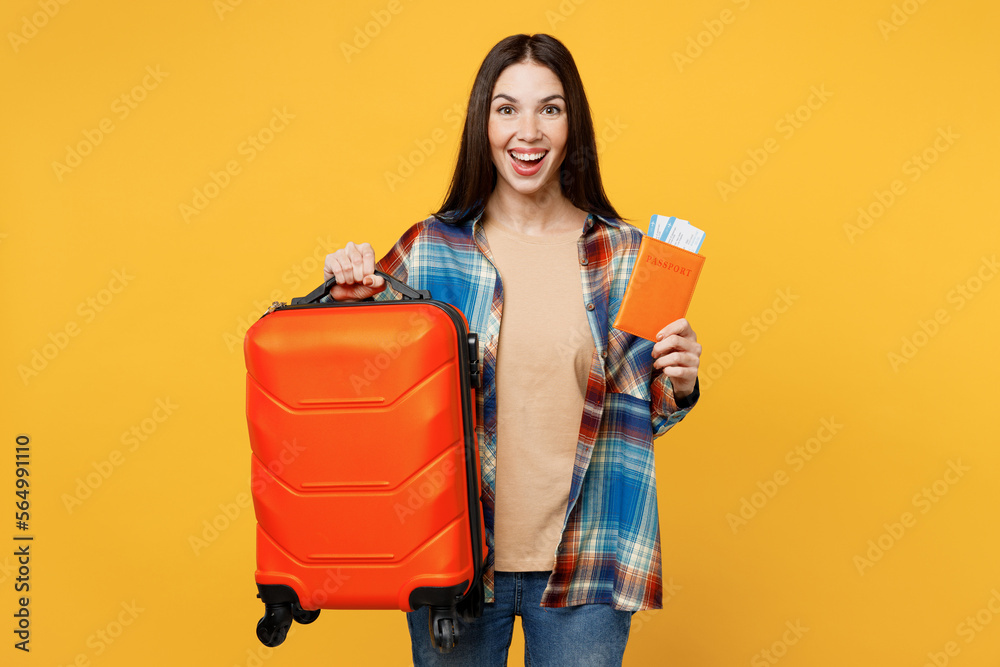 Wall mural Traveler happy woman wear casual clothes hold valise passport ticket isolated on plain yellow background studio. Tourist travel abroad in free spare time rest getaway. Air flight trip journey concept.