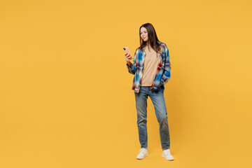 Full body young woman wear blue shirt beige t-shirt hold in hand use mobile cell phone browing internet chatting online isolated on plain yellow background studio portrait. People lifestyle concept.