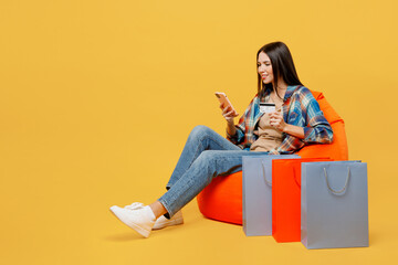 Full body young woman in blue shirt beige t-shirt sit in bag chair use mobile cell phone hold...
