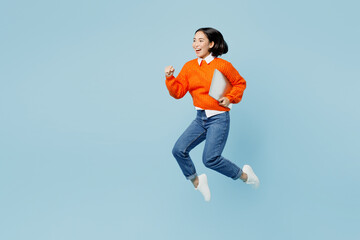 Full body side view excited young IT woman of Asian ethnicity wear orange sweater glasses jump high...