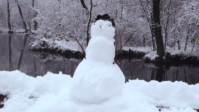 A snowman on the river bank in the middle of the European forest with gentle snowfall - trucking shot