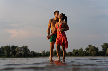 Young couple in love enjoying the sunset on the river beach. A beautiful couple walking and relaxing on a river beach near the city after a hard day on work.