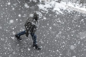 People walks on the urban city street on a snowy winter day with small white snow snowflakes in foreground