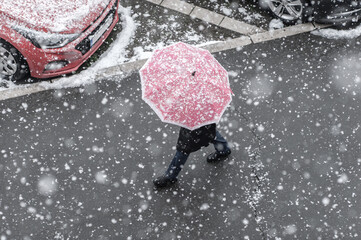 People walks on the urban city street on a snowy winter day with small white snow snowflakes in...