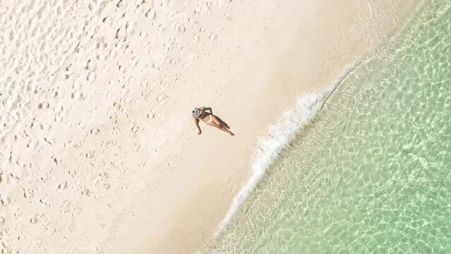 Above view with woman body in bikini sunbathing as laying on the beach, blue sea water in background -Summer fashion concept
