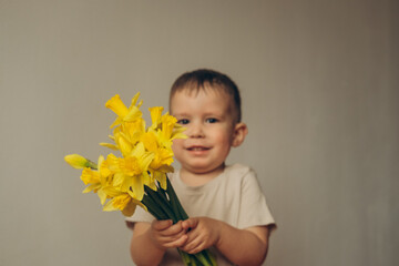 little boy holding and giving bouquet of bright yellow daffodils flowers hiding his face behind it.