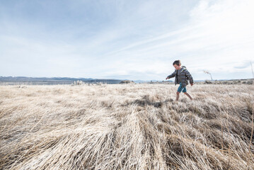 Boy walking alone on grass surrounding Mono Lake, California, USA