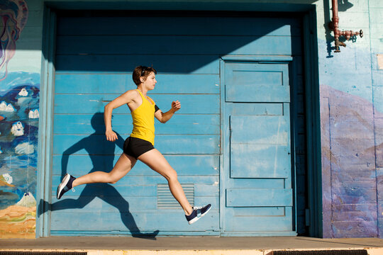 Woman runs and leaps in front of a big blue door in San Diego, California.