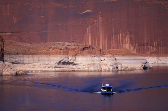 A houseboat moves away from the water's edge and a cliff.