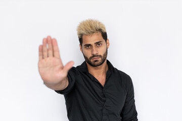 Portrait of confident young man making stop gesture over white background. Caucasian guy with stubble and highlighted hair wearing black T-shirt showing denial sign. Forbiddance concept