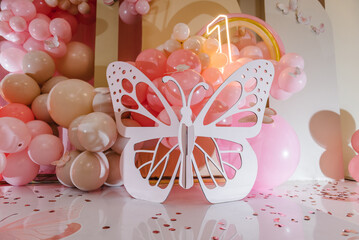 Birthday party for 1 year old girl on a background photo wall. Arch decorated pink balloons, rainbow, neon number one, confetti, paper decor and wooden white butterfly. Closeup. Children's photo zone.