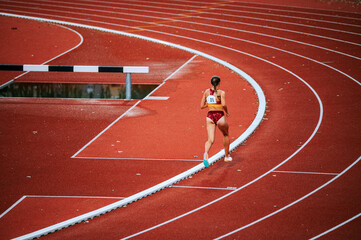 Determined female athlete in the midst of a distance race on track. Perfect for promoting perseverance, athleticism and physical fitness
