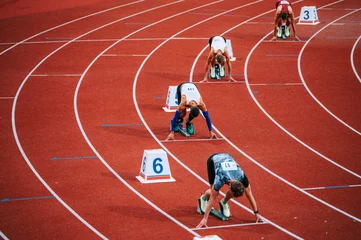 Tuinposter Powerful image of male athletes at the starting line of a 400m race on track. Suitable for sports and fitness campaigns, highlighting determination and focus © kovop58
