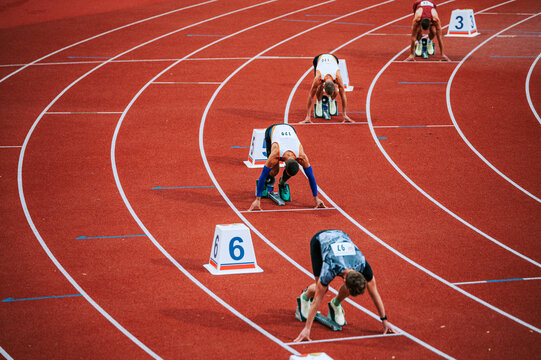 Powerful image of male athletes at the starting line of a 400m race on track. Suitable for sports and fitness campaigns, highlighting determination and focus