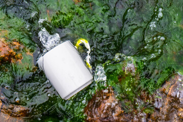 Fototapeta premium A Coffee mug laying out on the top of some rocks that covered with moss while the water keep splashing over it