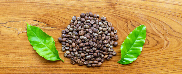 Top view of  Brown medium roasted coffee beans and green coffee leaf  on wooden background