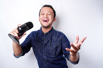 Portrait of carefree Asian man, having fun karaoke, singing in microphone while standing over white background