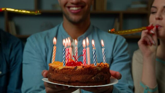 Cropped view African american 30s man hold birthday cake with burning candles two diverse friends blowing party whistles surprising male with festive event congratulate fun celebration make surprise