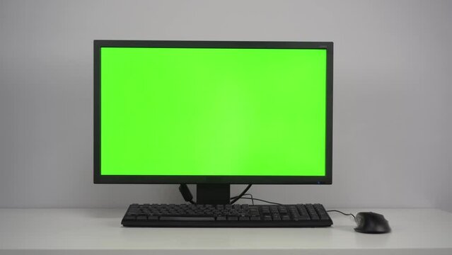A monitor with a green screen is on the desktop in the office. Chroma Key on PC. The camera is moving away from the object.