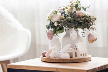 A beautiful postcard. The concept of the Bright Easter holiday. Flowers, rabbits, Easter eggs and Scandinavian white houses on a wooden table in a cozy living room.