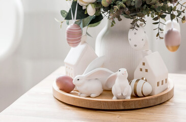 A beautiful postcard. The concept of the Bright Easter holiday. Flowers, rabbits, Easter eggs and Scandinavian white houses on a wooden table in a cozy living room.