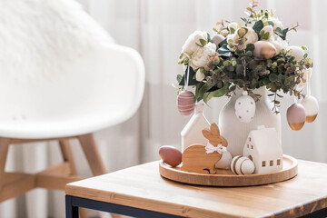 A beautiful postcard. The concept of the Bright Easter holiday. Flowers, rabbits, Easter eggs and Scandinavian white houses on a wooden table in a cozy living room.