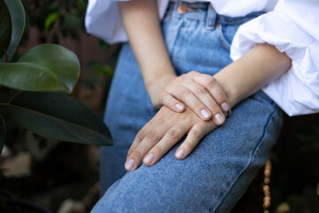Young well-groomed hands with natural manicure of a girl in a white blouse and blue jeans.