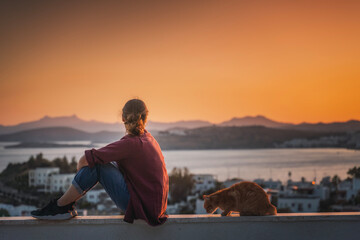 Dreamy young woman sitting on the roof and watching the beautiful sunset over sea and city