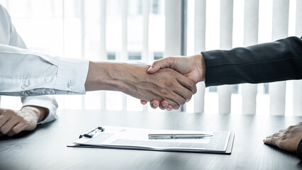 Man employer is shaking hands to congratulate the new employee after successful job interview and signing the contract in meeting room at office