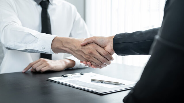 Man employer is shaking hands to congratulate the new employee after successful job interview and signing the contract in meeting room at office