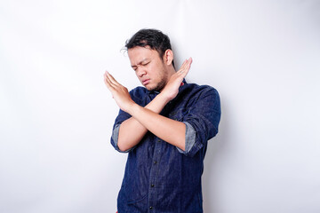 Handsome Asian man wearing blue shirt with hand gesture pose rejection or prohibition with copy...