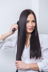 Fototapeta premium Young woman combing her long dark hair with a comb in a beauty salon , woman's hair in beauty salon, hairstyle concept