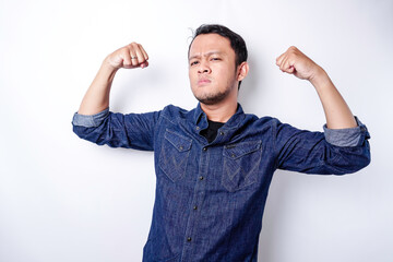 Fototapeta premium Excited Asian man wearing a blue shirt showing strong gesture by lifting his arms and muscles smiling proudly
