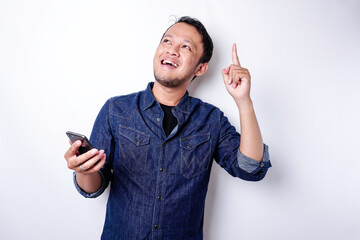A portrait of a happy Asian man wearing a blue shirt and holding her phone, isolated by white...