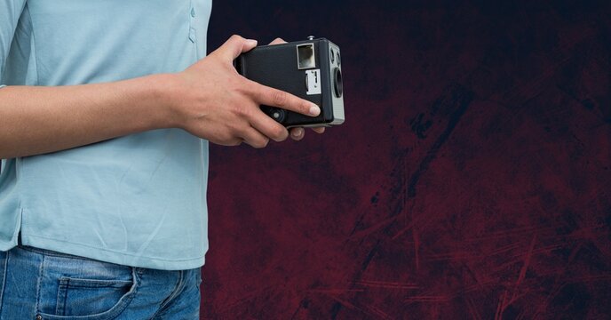 Mid section of a man holding a retro camera against copy space on grunge textured red background