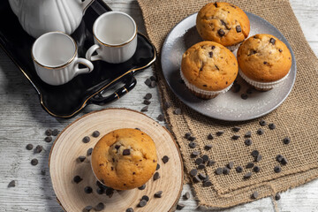 Muffin or cupcake with chocolate chips on wooden table background. Concept of making industrial or homemade pastries.