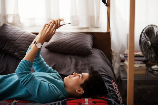 Side view of man using smart phone while lying on bed at home