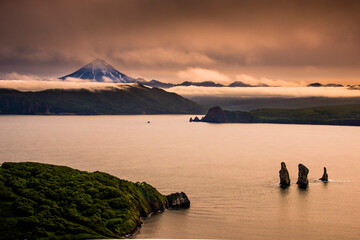 Water, rock formations and volcano with low hanging fog.  Kamchatka, Russia.