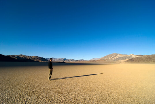 A man stands on The Racetrack looking at his long shadow on the sand in Death Valley National Park, CA.